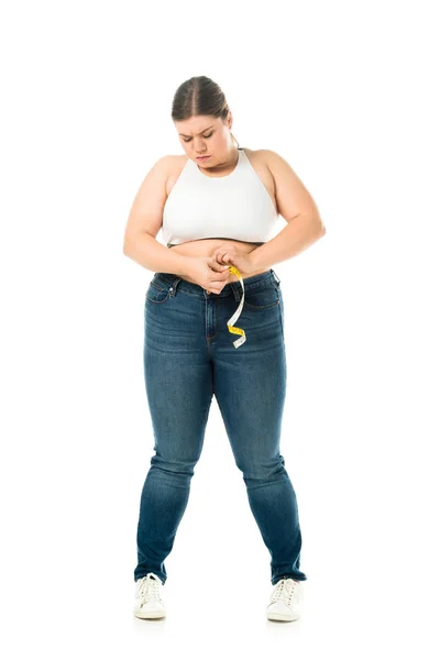 Perturbar mulher com excesso de peso em jeans medir a cintura com fita métrica isolada no branco, perder conceito de peso — Fotografia de Stock