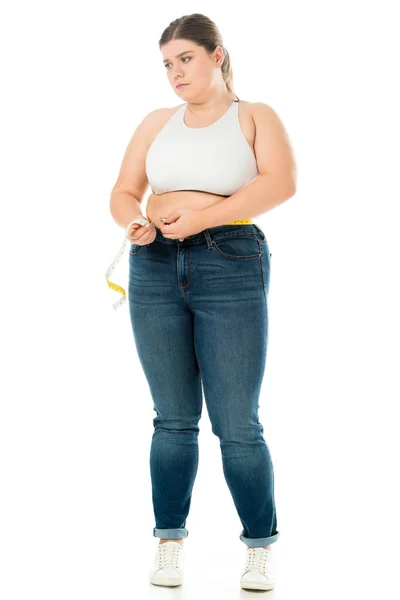 Dissatisfied overweight woman  in jeans measuring waist with measuring tape isolated on white, lose weight concept — Stock Photo