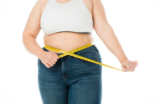 Обрізаний вид надмірної ваги жінки в джинсах вимірювальна талія з вимірювальною стрічкою ізольовано на білому фоні, концепція схуднення — стокове фото