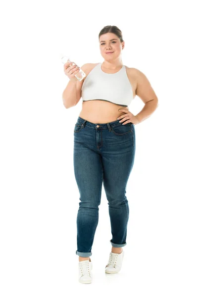 Smiling overweight woman in jeans holding bottle with water isolated on white — Stock Photo