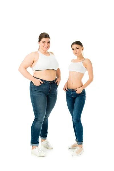 Lächelnde übergewichtige und schlanke Frauen in Jeans posieren mit Händen in Taschen isoliert auf weißem, Body Positivity Konzept — Stockfoto