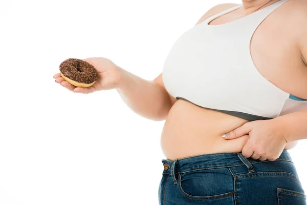 Vista recortada de la mujer con sobrepeso sosteniendo donut dulce y tocando el vientre aislado en blanco, concepto de dieta - foto de stock