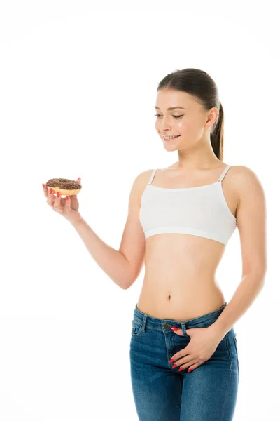 Smiling slim woman looking at sweet delicious doughnut isolated on white — Stock Photo