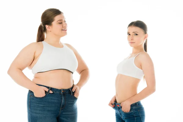 Schlanke und übergewichtige Frauen in Jeans posieren mit Händen in Taschen zusammen isoliert auf weiß, Body Positivity Konzept — Stockfoto