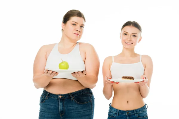 Happy slim woman holding plate with doughnut and upset overweight woman holding plate with green apple isolated on white — Stock Photo