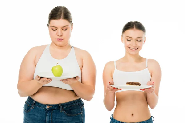 Щаслива струнка жінка дивиться на тарілку з пончиком і сумною надмірною вагою жінка дивиться на тарілку з зеленим яблуком ізольовано на білому — стокове фото