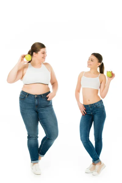 Felizes mulheres magras e com excesso de peso com maçãs verdes olhando umas para as outras isoladas em branco — Fotografia de Stock