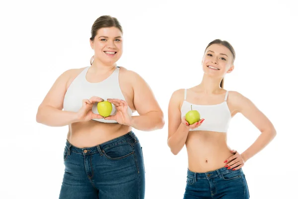 Glückliche schlanke und übergewichtige Frauen mit grünen Äpfeln, die isoliert auf weiß in die Kamera schauen — Stockfoto