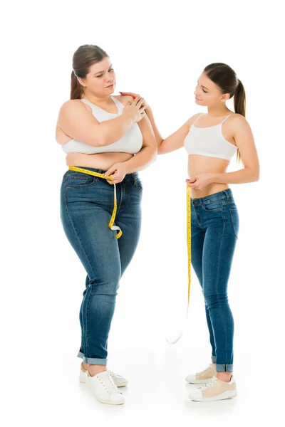 Mujer delgada apoyando triste mujer con sobrepeso con cinta métrica aislada en blanco - foto de stock