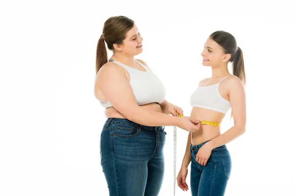 Felice donna in sovrappeso che misura la vita della donna magra isolata sul bianco — Foto stock