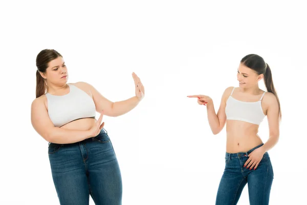 Sonriente en forma mujer señalando con el dedo a la mujer triste con sobrepeso haciendo stop gesto aislado en blanco - foto de stock