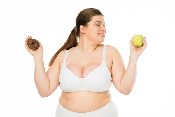 Happy young overweight woman in underwear holding doughnut and green apple isolated on white — Stock Photo