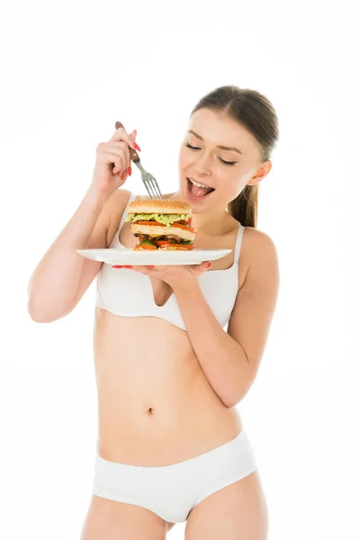 Mince belle femme en sous-vêtements manger hamburger savoureux avec fourchette de la plaque isolée sur blanc — Photo de stock