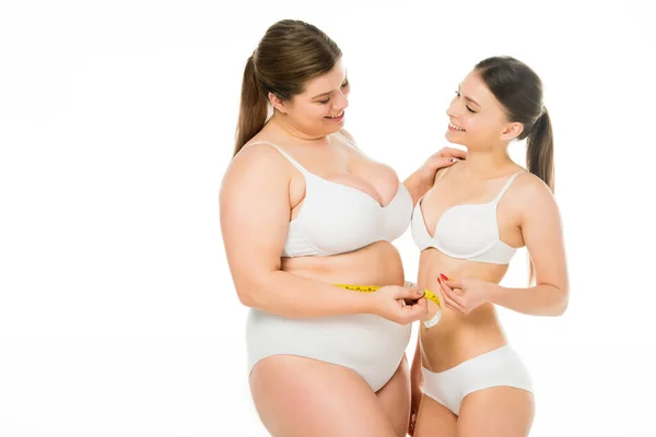 Happy body positive overweight woman looking at slim woman while holding measuring tape together isolated on white — Stock Photo