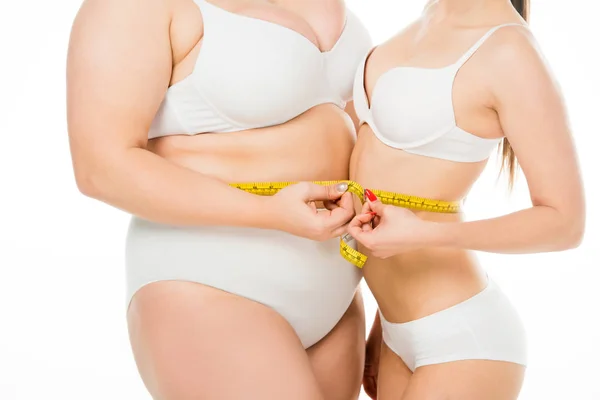 Обрізаний вид на тіло позитивної надмірної ваги жінка і струнка жінка тримає вимірювальну стрічку разом ізольовано на білому — стокове фото