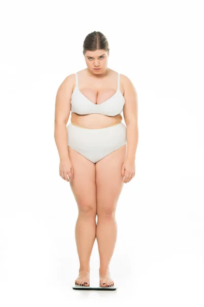 Грустная молодая женщина с избыточным весом, стоящая на весах изолированная на белом, похудеть концепция — стоковое фото