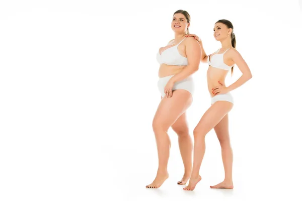 Felices mujeres delgadas y con sobrepeso en ropa interior posando juntos aislados en blanco, concepto de positividad corporal - foto de stock