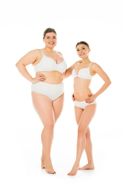 Felices mujeres delgadas y alegres con sobrepeso en ropa interior posando juntos aislados en blanco, concepto de positividad corporal - foto de stock
