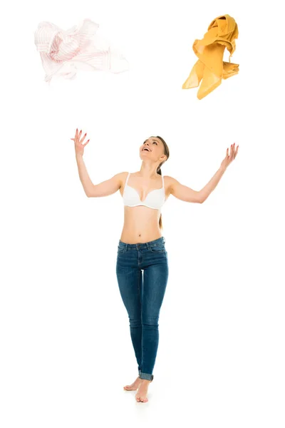 Slim woman in underwear and blue jeans throwing up and looking at clothing isolated on white — Stock Photo