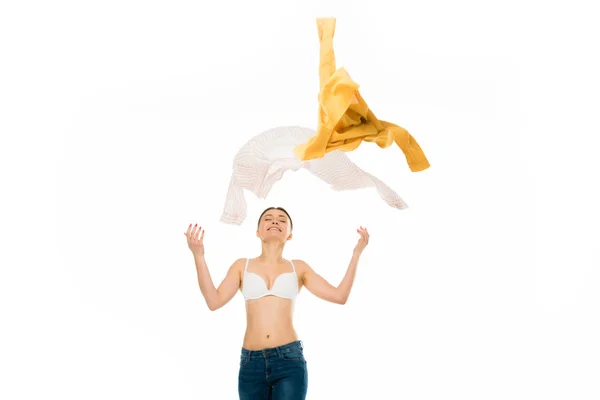 Slim happy woman in underwear and blue jeans throwing up clothing isolated on white — Stock Photo