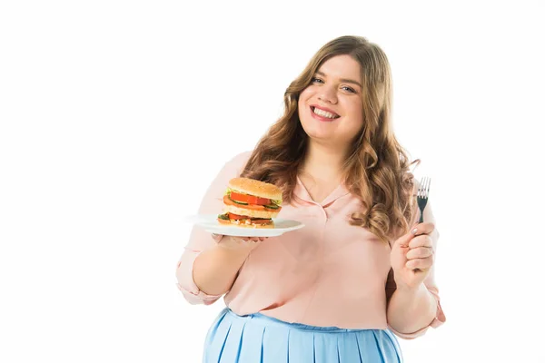 Щаслива усміхнена жінка тримає смачний бургер на тарілці і виделці ізольована на білому — стокове фото
