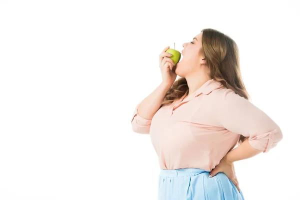 Вид збоку надмірної ваги жінка кусає зелене яблуко ізольовано на білому — стокове фото