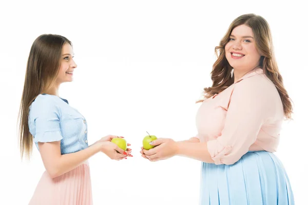 Lächelnd elegante, übergewichtige und schlanke Frauen, die Äpfel isoliert auf Weiß halten — Stockfoto