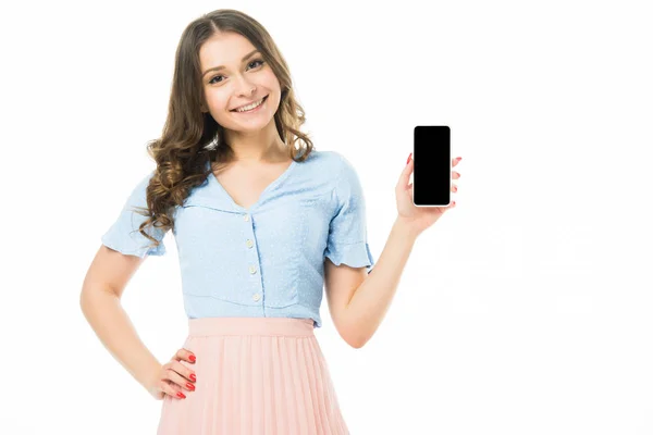 Улыбающаяся красивая девушка показывает смартфон с пустым экраном и глядя на камеру изолированы на белом — стоковое фото