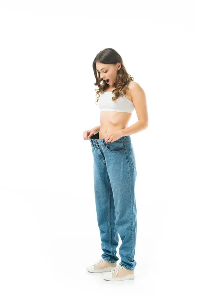Surprise mince fille regardant gros jeans isolés sur blanc, perdre du poids concept — Photo de stock