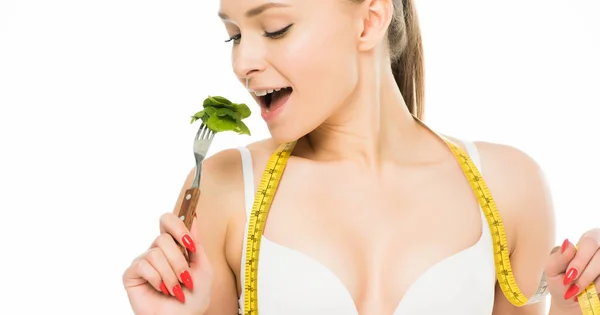 Belle femme avec ruban à mesurer manger des feuilles d'épinards verts isolé sur blanc, concept de régime — Photo de stock