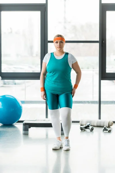 Übergewichtige Frau steht in Sportbekleidung neben Fitnessball und Hanteln — Stockfoto