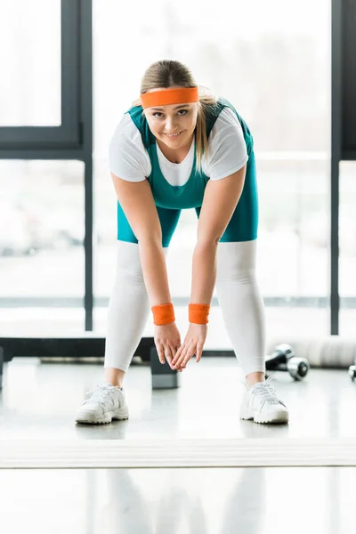 Mulher com sobrepeso alegre alongamento em sportswear no ginásio — Fotografia de Stock