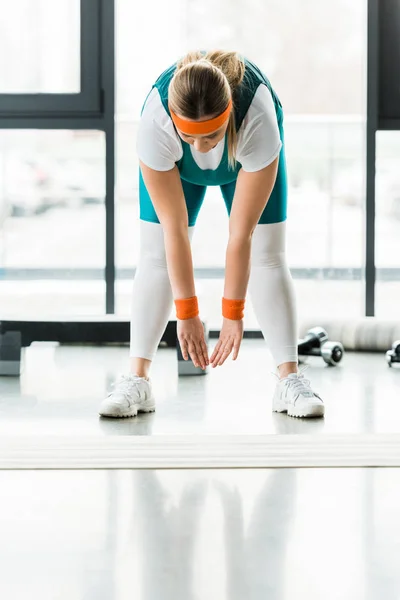 Overweight woman stretching in sportswear near fitness mat — Stock Photo