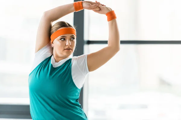 Overweight woman stretching while standing in sportswear in gym — Stock Photo