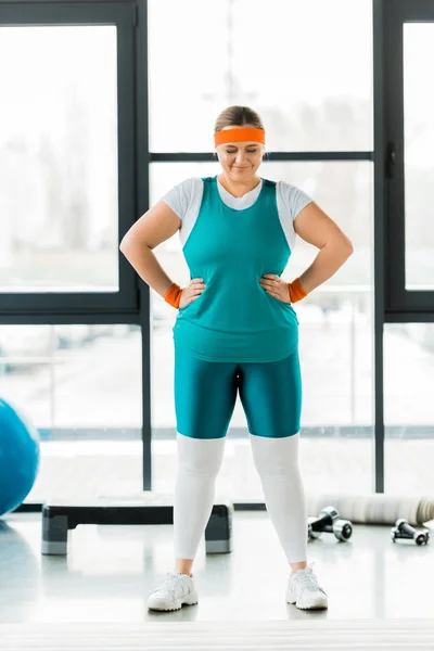 Plus-Size-Frau steht und lächelt neben Fitnessmatte im Fitnessstudio — Stockfoto