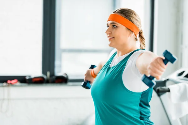 Enfoque selectivo de feliz mujer con sobrepeso haciendo ejercicio en ropa deportiva con mancuernas - foto de stock