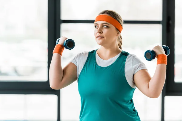 Alegre mujer con sobrepeso haciendo ejercicio con mancuernas en el gimnasio - foto de stock
