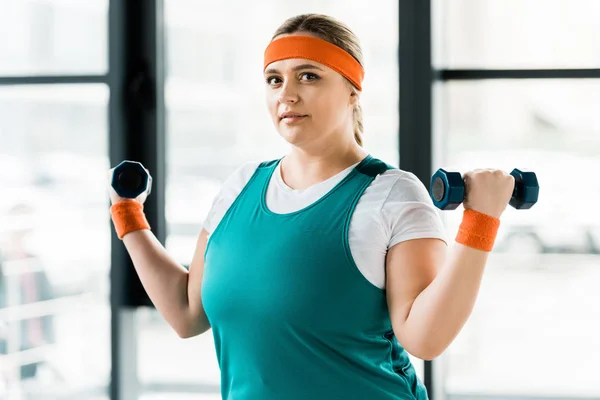 Atractiva mujer de tamaño grande haciendo ejercicio con pesas en el gimnasio - foto de stock