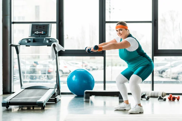 Feliz más mujer de tamaño haciendo ejercicio con pesas cerca de la cinta de correr - foto de stock