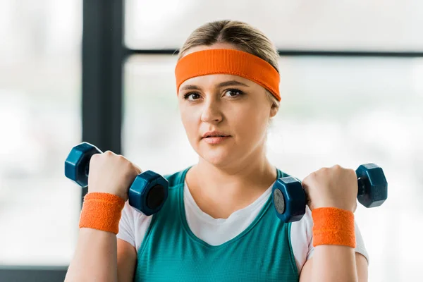 Beautiful plus size woman holding dumbbells in gym — Stock Photo