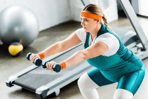 Зосереджена плюс розмір жінка тренування з гантелями в спортзалі — стокове фото