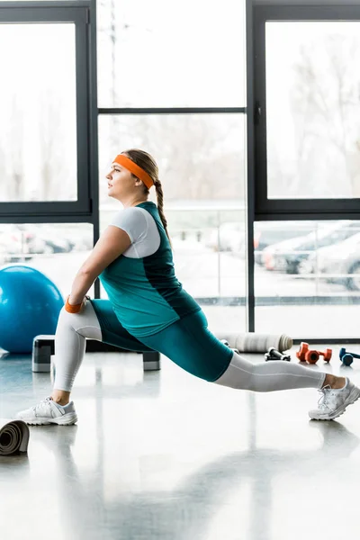 Confiant plus taille femme en vêtements de sport étirement dans la salle de gym — Photo de stock