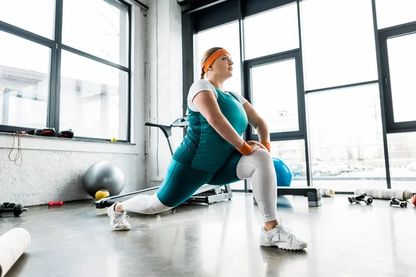 Plus size girl in sportswear stretching in gym — Stock Photo