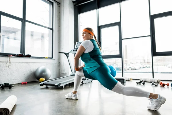 Attractive plus size girl in sportswear stretching in gym — Stock Photo