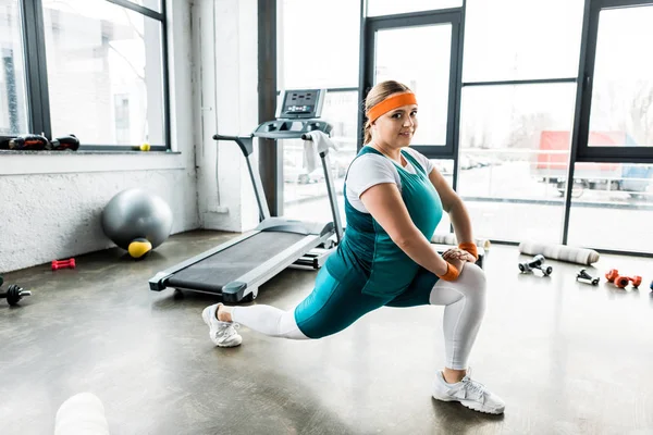 Happy plus size girl in sportswear stretching in gym — Stock Photo