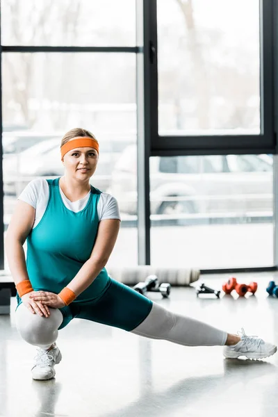 Attraktives Plus-Size-Girl in Sportbekleidung, das sich dehnt und im Fitnessstudio in die Kamera schaut — Stockfoto