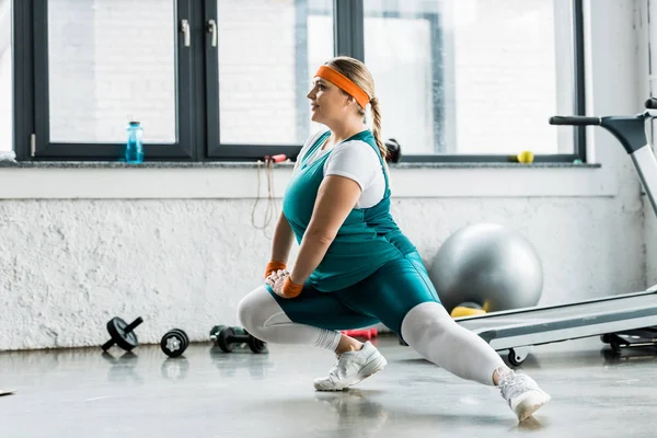 Smiling plus size girl in sportswear stretching in gym — Stock Photo