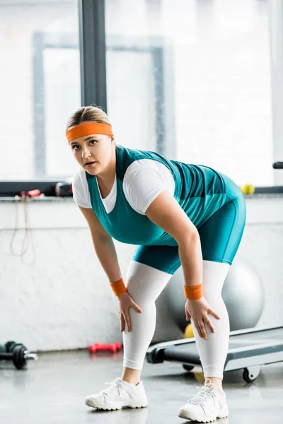 Plus Size Girl in Sportbekleidung Stretching und Blick in die Kamera im Fitnessstudio — Stockfoto