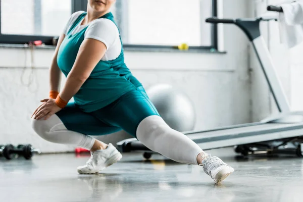 Cropped view of plus size girl in sportswear stretching in gym — Stock Photo