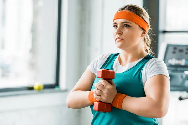 Serious overweight girl holding dumbbell in gym — Stock Photo